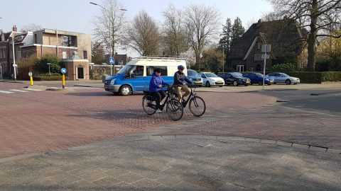 Senioren met helm op, op de fiets op kruispunt